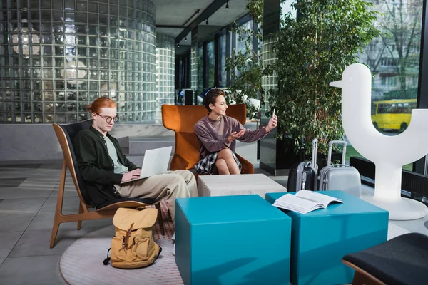 Young couple using laptop and smartphone near baggage in hotel lobby — Stock Photo