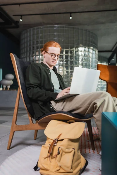 Redhead man using laptop near suitcase in hotel lobby — Stock Photo