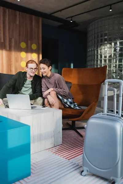 Positive travelers using devices near suitcases in hotel lobby — Stock Photo