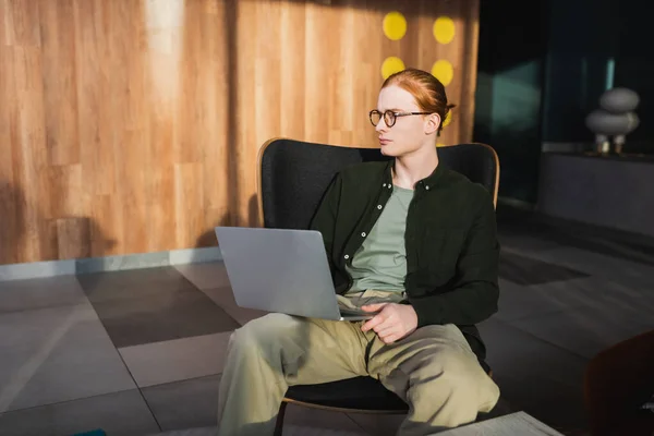 Jovem freelancer ruiva usando laptop no lobby do hotel — Fotografia de Stock