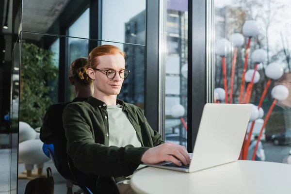 Red haired man in eyeglasses using laptop in hotel lobby — Stockfoto