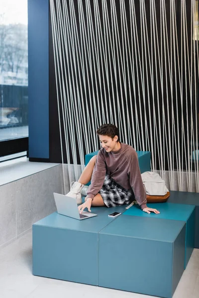 Smiling traveler using laptop near backpack in modern hotel lobby — Stock Photo