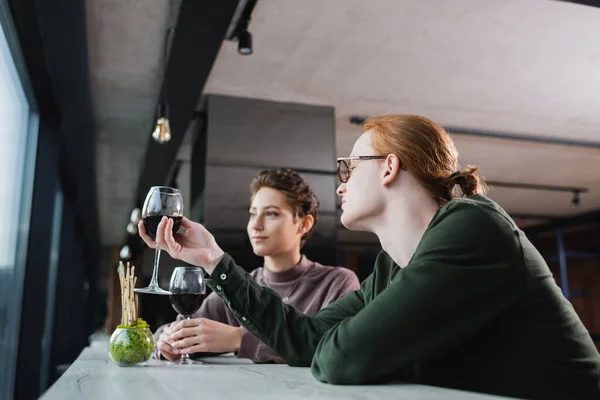 Jeune homme tenant du vin près de petite amie floue à l'hôtel — Photo de stock