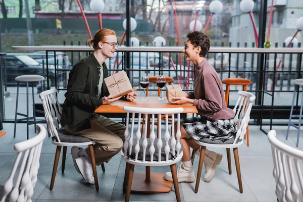 Young couple holding gifts near glasses of wine in hotel cafe — Stock Photo