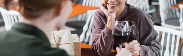 Обрізаний вид усміхненої пари тостів вина біля подарунків у готельному кафе, банер — стокове фото