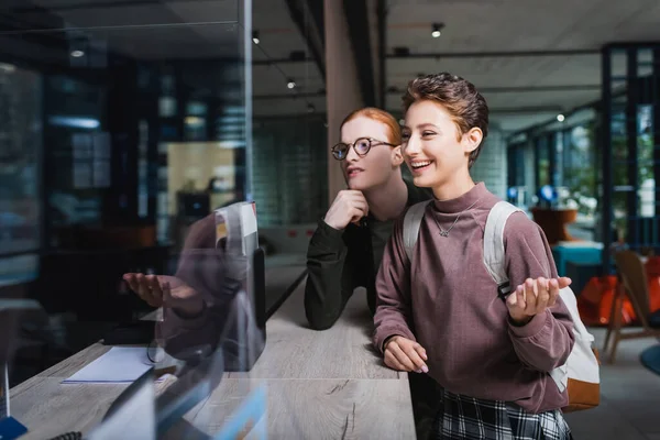 Mujer joven con mochila hablando cerca de novio y recepción del hotel — Stock Photo