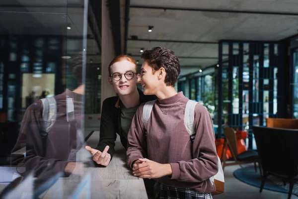 Cheerful travelers with backpack talking near hotel reception — Stockfoto