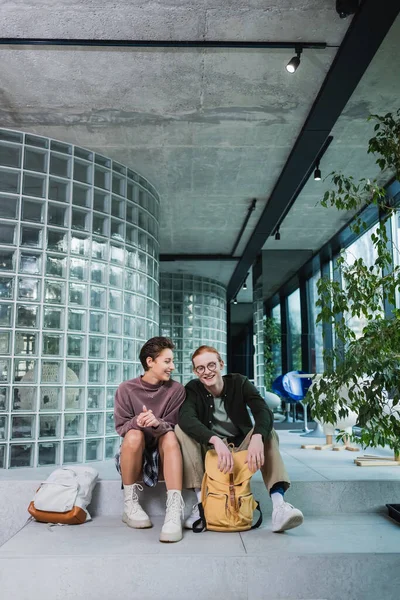 Lächelnde Frau spricht mit Freund in der Nähe von Rucksäcken auf Treppe im Hotel — Stockfoto