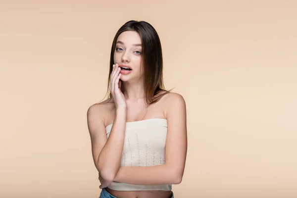 Young woman in crop top with bare shoulders and open mouth looking at camera isolated on beige — Stock Photo