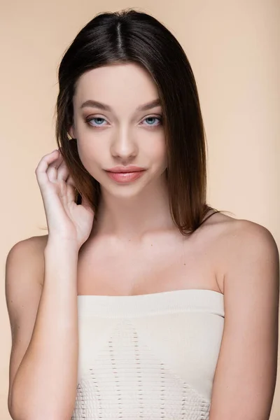 Young woman with bare shoulders adjusting hair isolated on beige — Foto stock