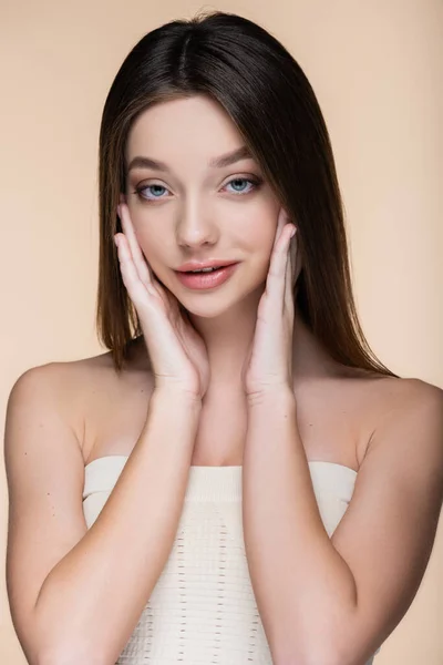 Young woman in crop top with bare shoulders touching cheeks isolated on beige — Stock Photo