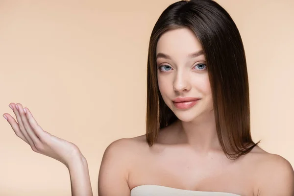 Hübsche junge Frau mit nackten Schultern, die mit der Hand isoliert auf beige zeigt — Stockfoto