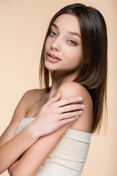 Brunette woman in crop top touching bare shoulders isolated on beige — Stockfoto