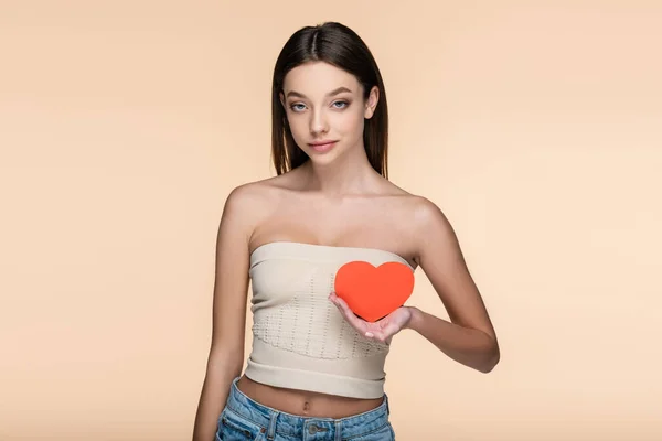 Giovane donna in crop top con spalle nude in possesso di cuore di cartone rosso isolato su beige — Foto stock