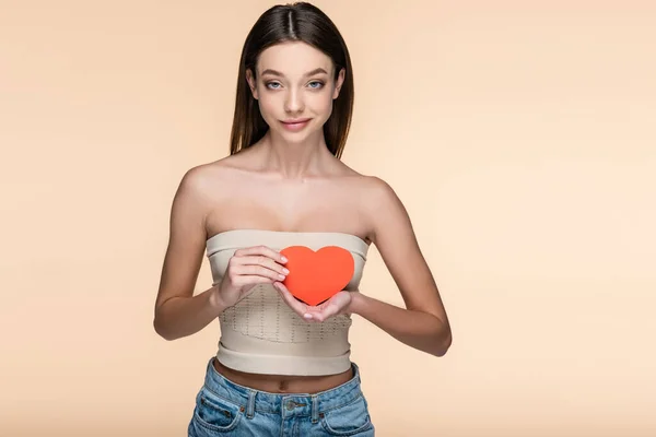 Positive woman in crop top with bare shoulders holding red paper heart isolated on beige — Stockfoto