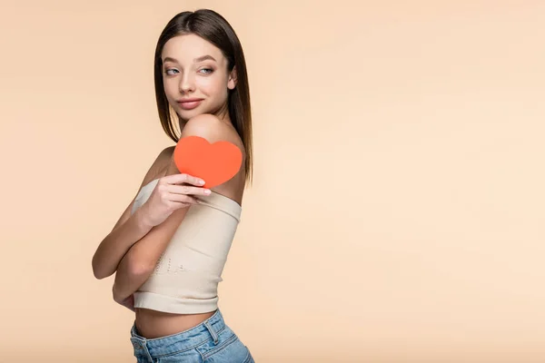 Mujer alegre en la parte superior de la cosecha sosteniendo corazón de papel rojo aislado en beige - foto de stock