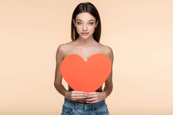 Happy woman with bare shoulders covering body with red paper heart isolated on beige — Stock Photo