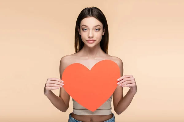 Brunette woman with bare shoulders holding red paper heart isolated on beige — Stock Photo