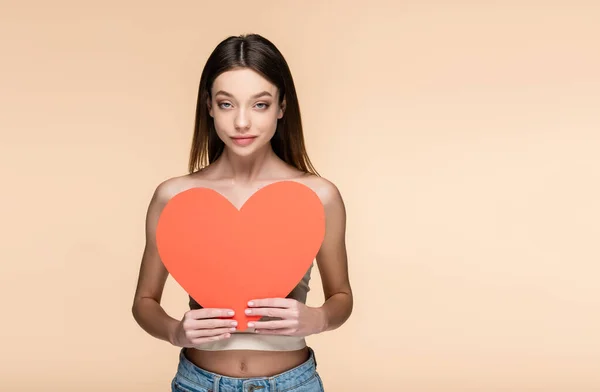 Young woman with bare shoulders holding red paper heart isolated on beige — Stock Photo