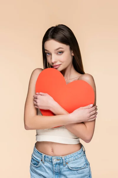 Happy woman in crop top hugging red paper heart isolated on beige — Stock Photo