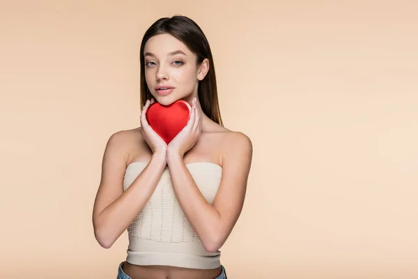 Brunette woman holding red heart-shaped metallic box isolated on beige — Stock Photo