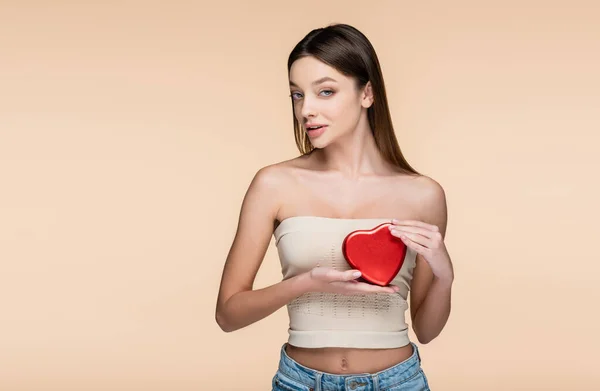 Morena mujer sosteniendo rojo en forma de corazón caja aislada en beige — Stock Photo