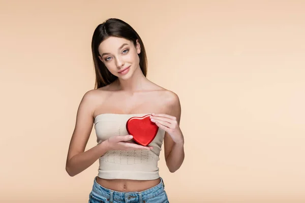 Zufriedene Frau hält rote herzförmige Metallschachtel isoliert auf beige — Stockfoto