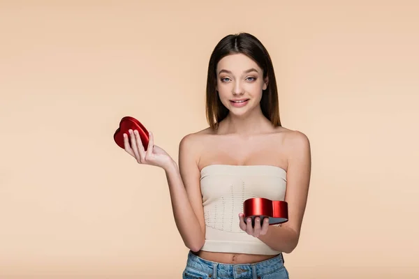 Happy young woman holding heart-shaped red box isolated on beige — Fotografia de Stock