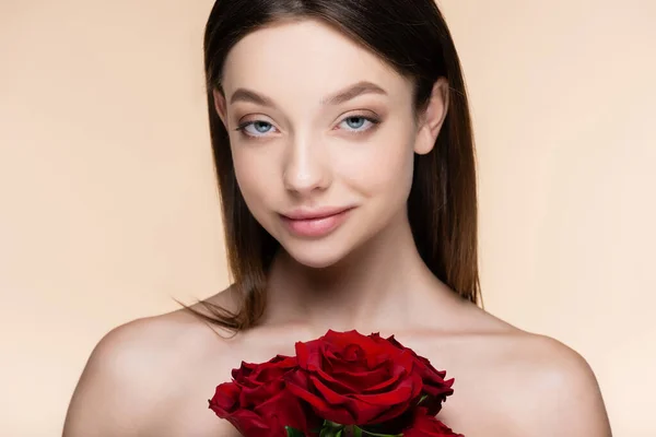 Jovem com ombros nus perto de buquê de rosas vermelhas isoladas em bege — Fotografia de Stock