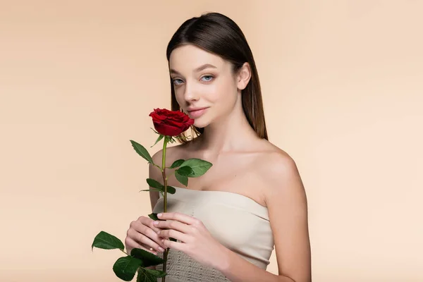 Young woman with bare shoulders holding red rose isolated on beige — Fotografia de Stock