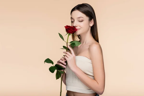 Young woman with closed eyes smelling red rose isolated on beige — Stock Photo