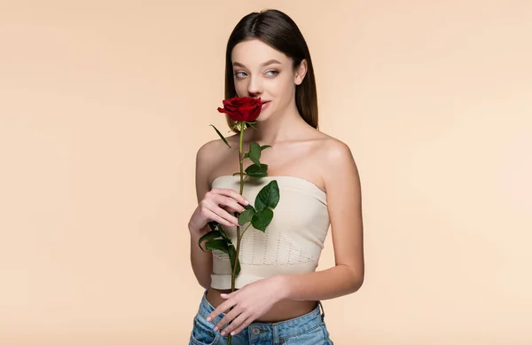 Young woman in crop top smelling red rose isolated on beige — Stock Photo
