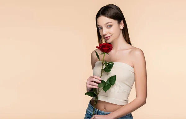Brünette junge Frau mit nackten Schultern, rote Rose vereinzelt auf beige haltend — Stockfoto