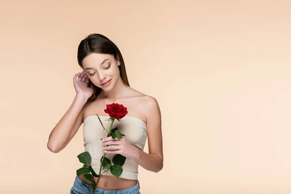 Sinnliche junge Frau mit nackten Schultern, die auf rote Rose in Beige blickt — Stockfoto