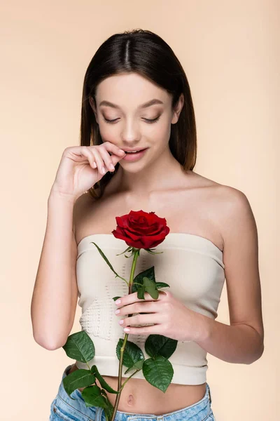 Flirty woman with bare shoulders holding red rose isolated on beige — Foto stock