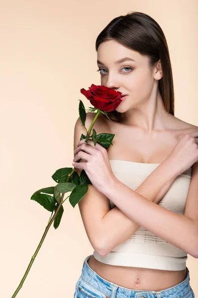 Young woman with bare shoulders smelling aromatic rose isolated on beige — стоковое фото