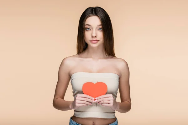 Femme sensuelle dans le haut de la culture avec épaules nues tenant coeur coupé en papier rouge isolé sur beige — Photo de stock