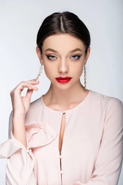 Jolie femme avec des lèvres rouges regardant caméra tout en touchant boucle d'oreille isolé sur gris — Photo de stock