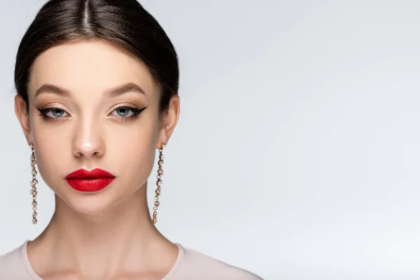 Hübsche Frau mit Ohrringen und hellem Make-up blickt vereinzelt in die Kamera auf grau — Stockfoto