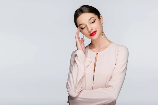 Mujer complacida en pendientes y blusa posando aislada sobre gris - foto de stock