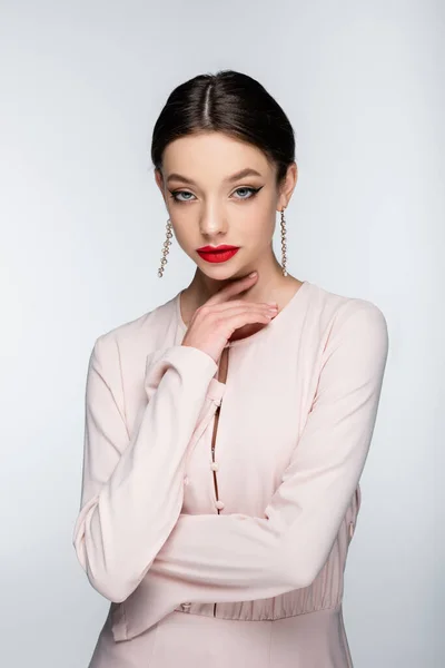 Young woman in earrings and blouse looking at camera while posing isolated on grey — стоковое фото