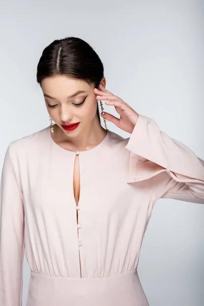 Pretty woman in earrings and blouse looking down while posing isolated on grey — стоковое фото