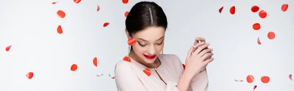 Young and happy woman near falling rose petals on grey, banner — стоковое фото