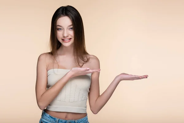 Mujer joven y alegre en la parte superior de la cosecha señalando con las manos aisladas en beige - foto de stock