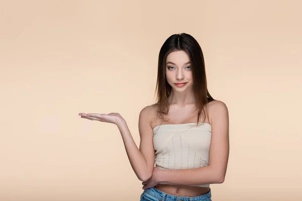 Young and pretty woman in crop top pointing with hand isolated on beige — стоковое фото