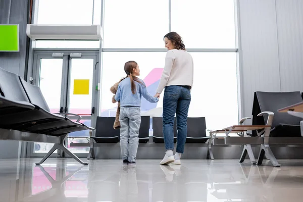 Happy mother and daughter holding hands while looking at each other in airport lounge — стоковое фото