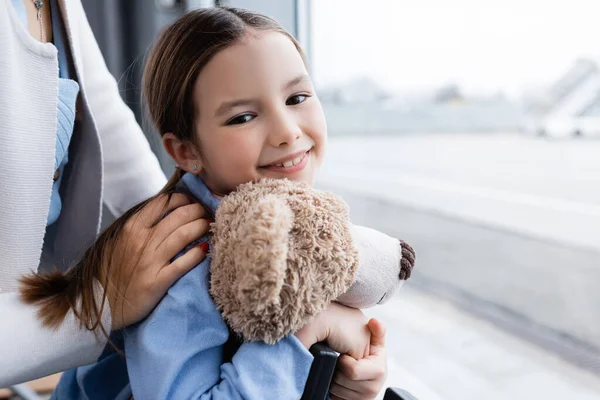 Задоволена дитина тримає м'яку іграшку біля вікна матері та аеропорту — стокове фото