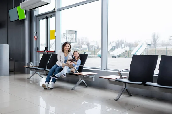 Happy mother and daughter sitting in airport lounge hall - foto de stock