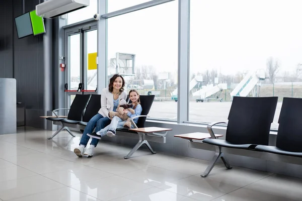 Happy mother and daughter sitting in airport lounge hall — Stockfoto