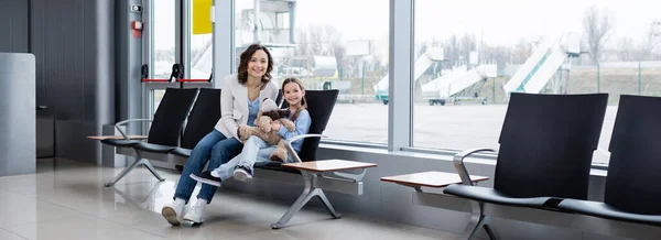 Happy mother and daughter sitting in airport lounge hall, banner — Fotografia de Stock